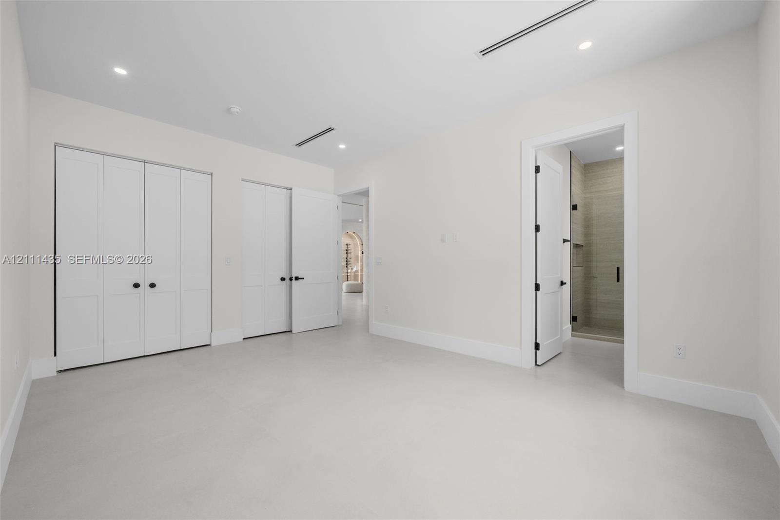 Room featuring smooth flooring, recessed lighting, double-door closet cabinetry, and a doorway revealing a tiled shower enclosure
