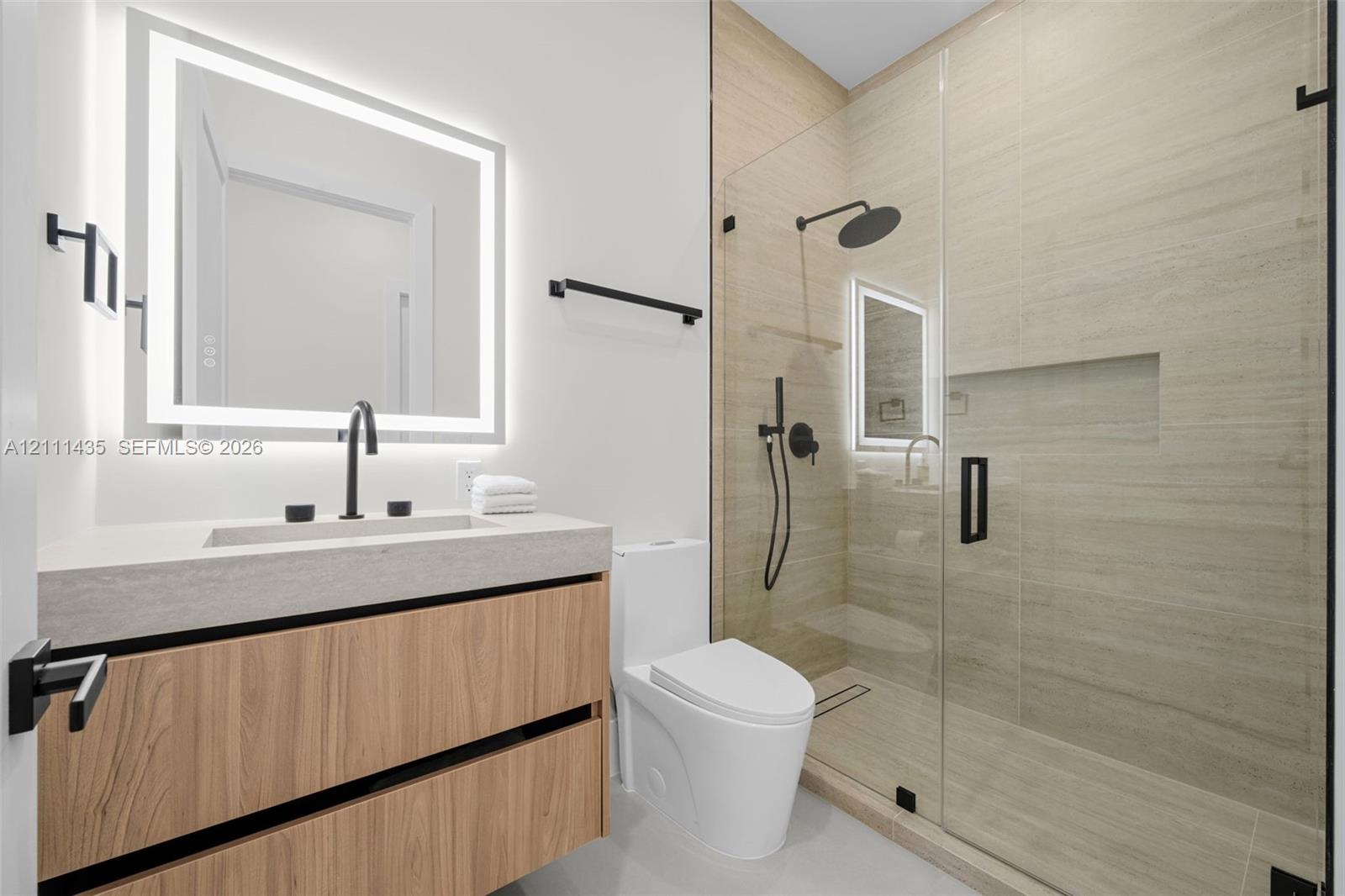 Floating wood-finish vanity with a rectangular sink, integrated LED-backlit mirror, walk-in shower with a glass enclosure and built-in recessed shelving, and matte black fixtures