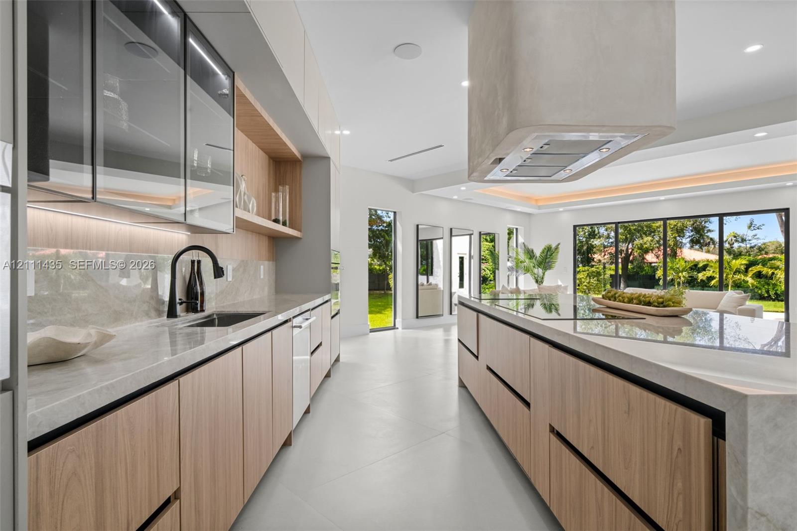 Kitchen featuring light wood-finish cabinetry, stone countertops, integrated under-cabinet lighting, a contemporary ceiling-mounted range hood, and large-format tile flooring