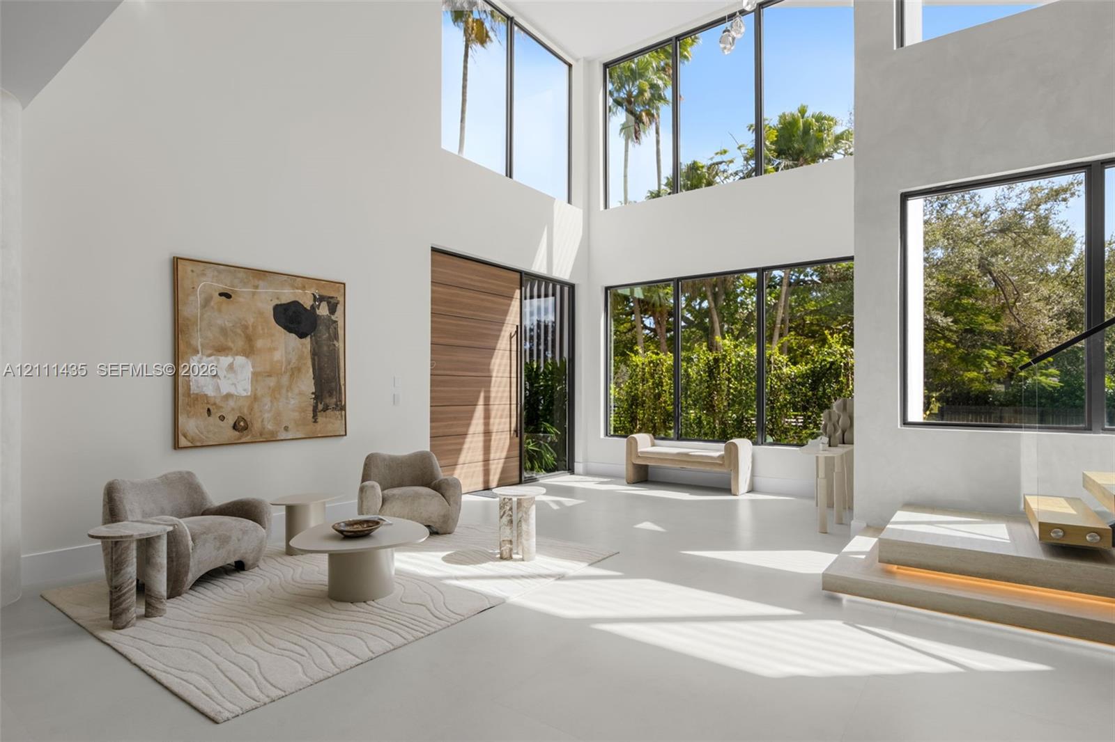 Double-height living area featuring floor-to-ceiling windows, polished concrete flooring, a natural wood entry door, and a floating staircase with integrated lighting