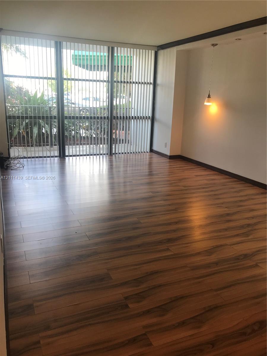 Floor-to-ceiling windows with vertical blinds, wood-finish flooring, and a recessed ceiling feature with a pendant light fixture