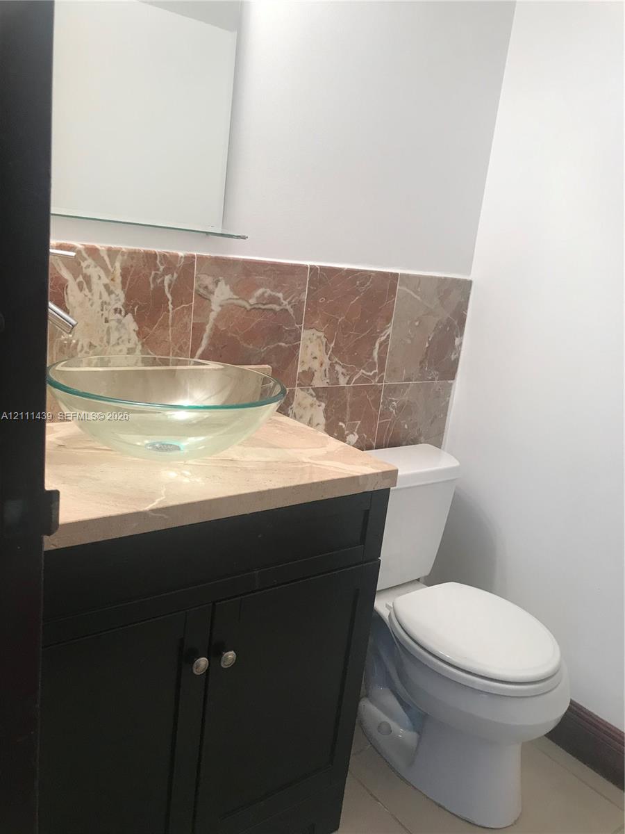 Half bathroom Dark finish vanity featuring a stone countertop, glass vessel sink, wall-mounted mirror, and decorative stone tile backsplash