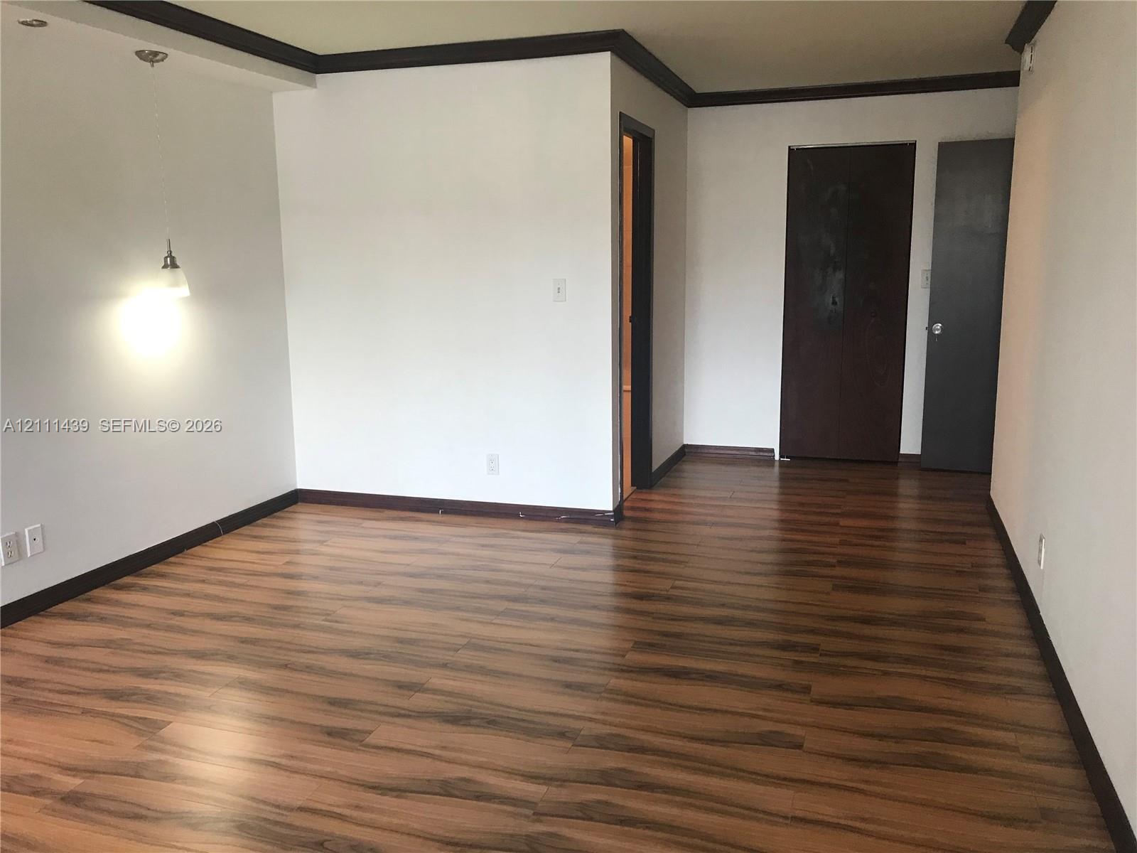 Wood-finish flooring, dark-toned interior door trim, crown molding, and a suspended pendant light fixture