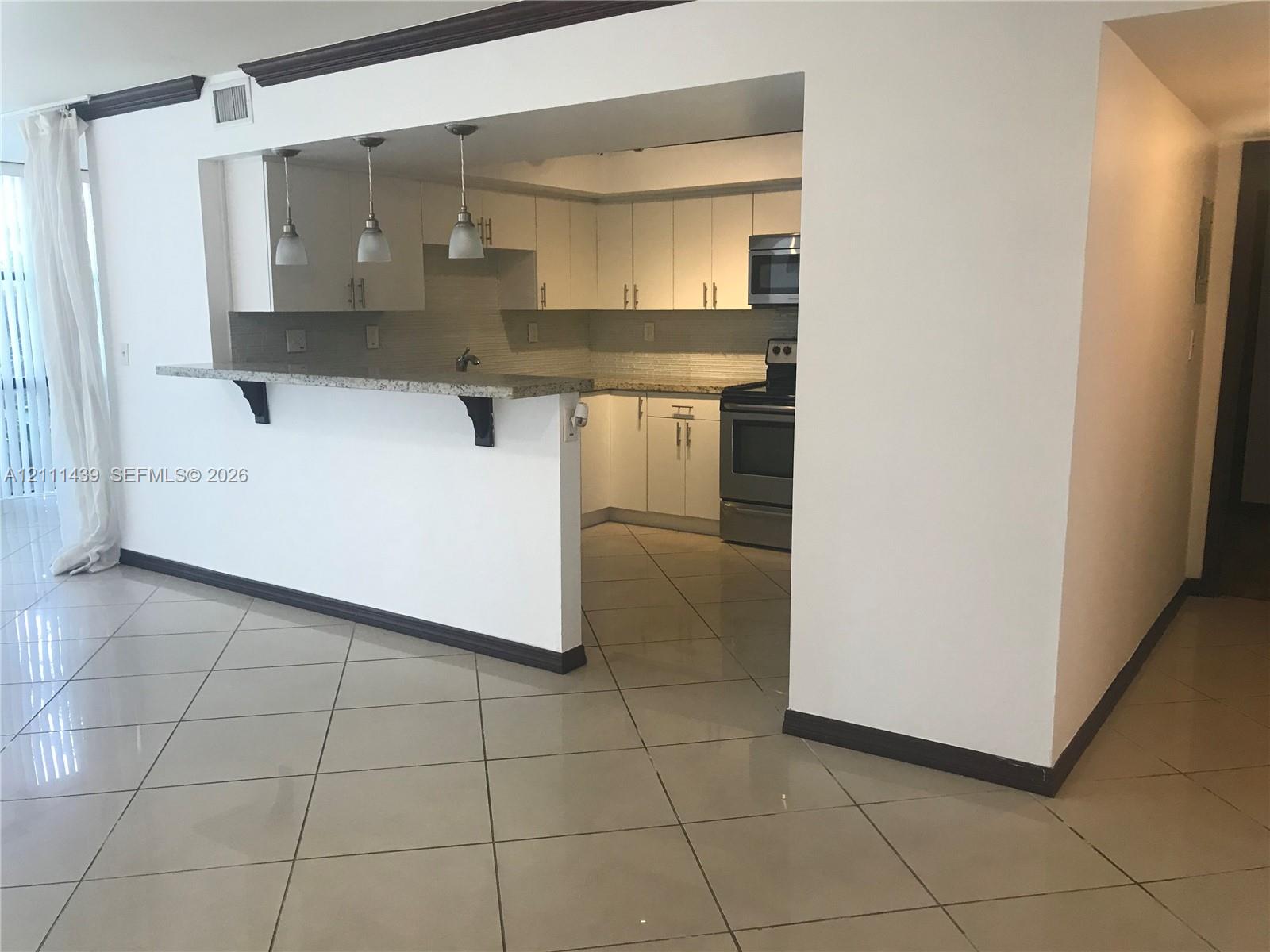 Kitchen featuring white cabinetry, stone-finish countertops, stainless steel appliance suite, tile flooring, and a breakfast bar with three pendant lights