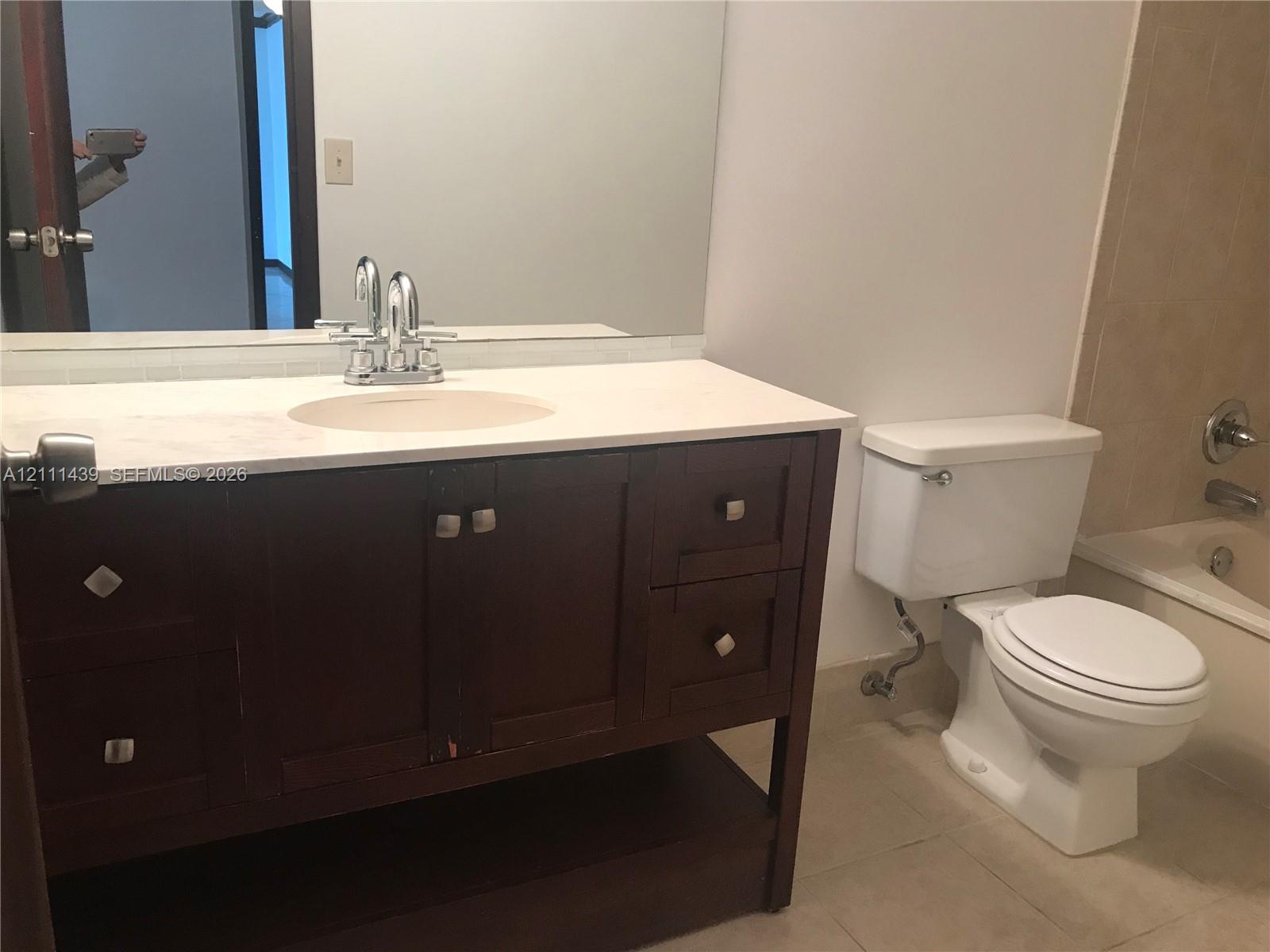 Dark wood vanity with a solid surface countertop, integrated sink basin, polished chrome faucet, and large rectangular wall-mounted mirror