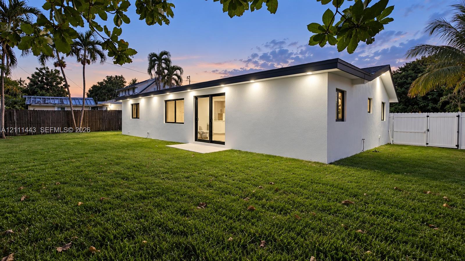 Expansive backyard featuring a level lawn, white perimeter fencing, and recessed exterior soffit lighting