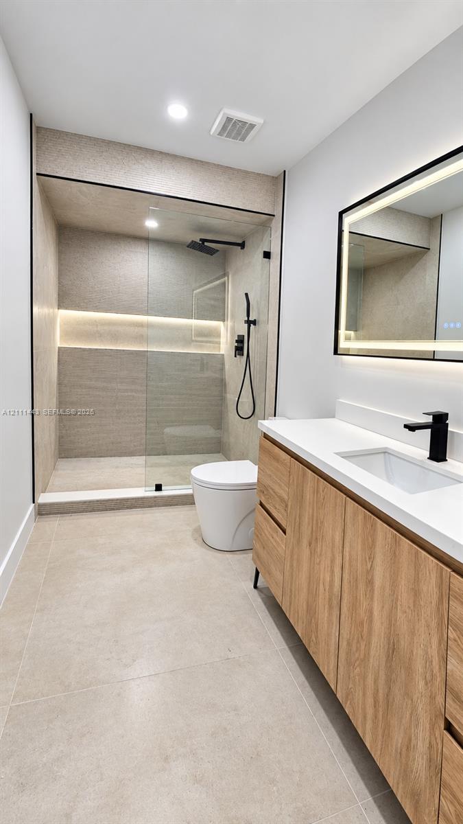 Walk-in shower with integrated wall lighting and matte black rainfall fixture, wood-finish floating vanity with quartz countertop, and rectangular LED-backlit mirror