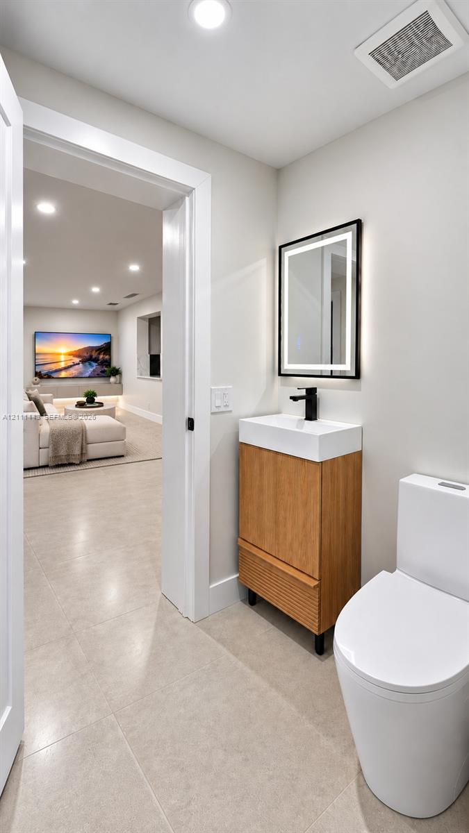 Digitally Staged - Bathroom featuring a wood-finish vanity with a rectangular sink, matte black faucet, illuminated mirror, and a dual-flush toilet