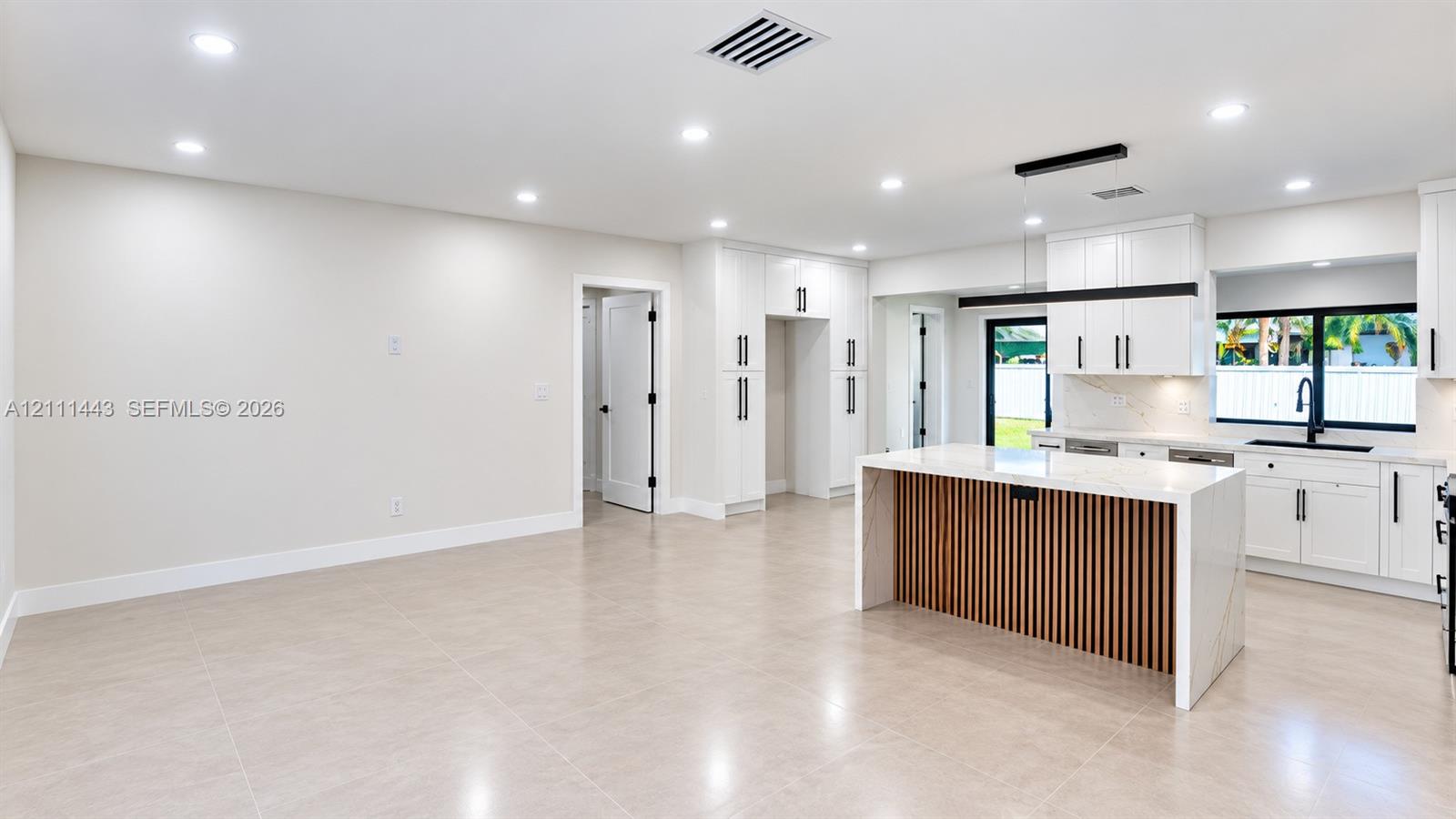 Kitchen featuring white shaker-style cabinetry, an island with wood-slat detailing and stone-surface countertop, recessed lighting, and large-format tile flooring