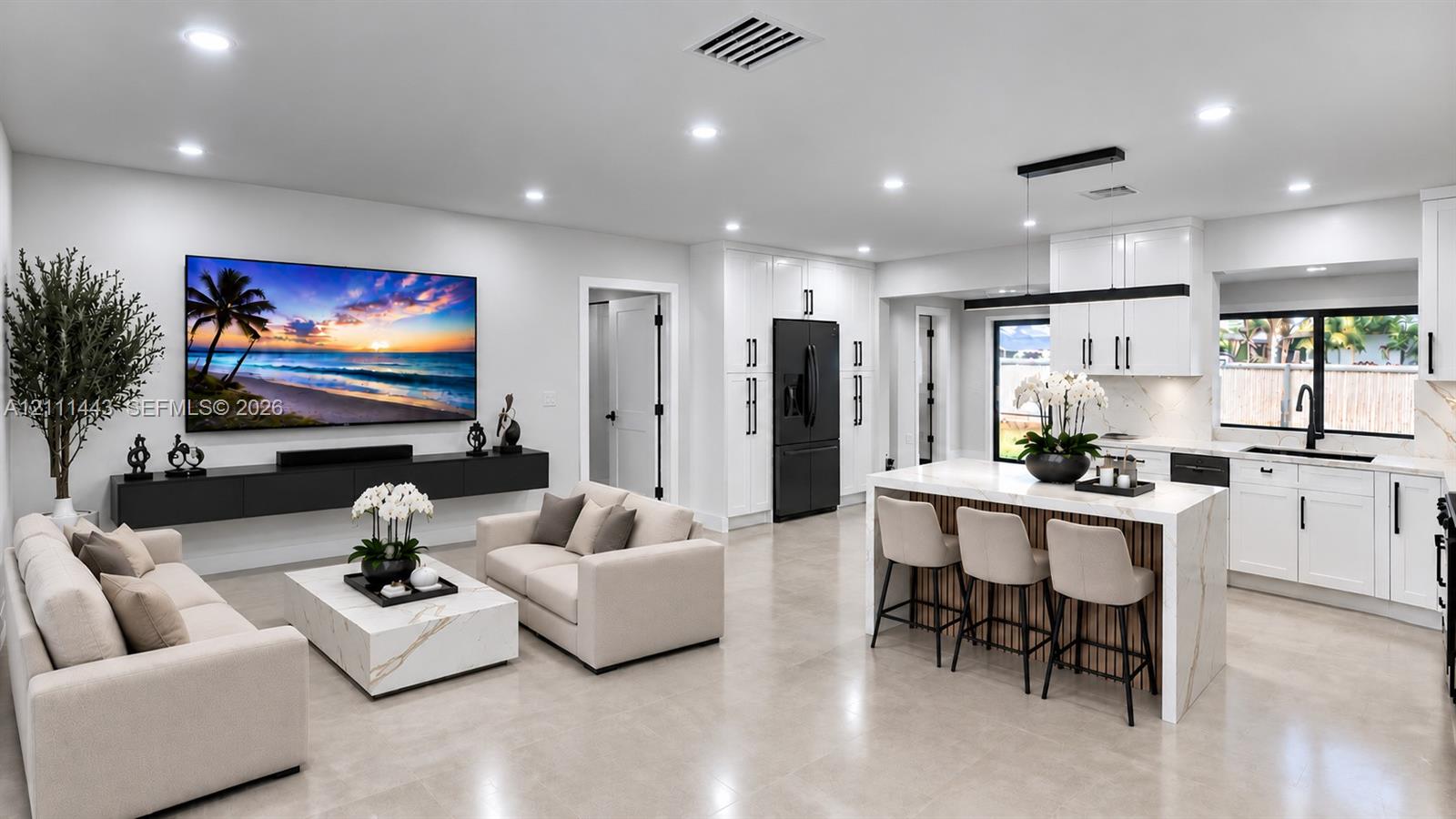Open-concept living space featuring high-gloss white cabinetry, a large kitchen island with stone-finish countertops, floating wall-mounted storage, recessed lighting, and large-format tile flooring