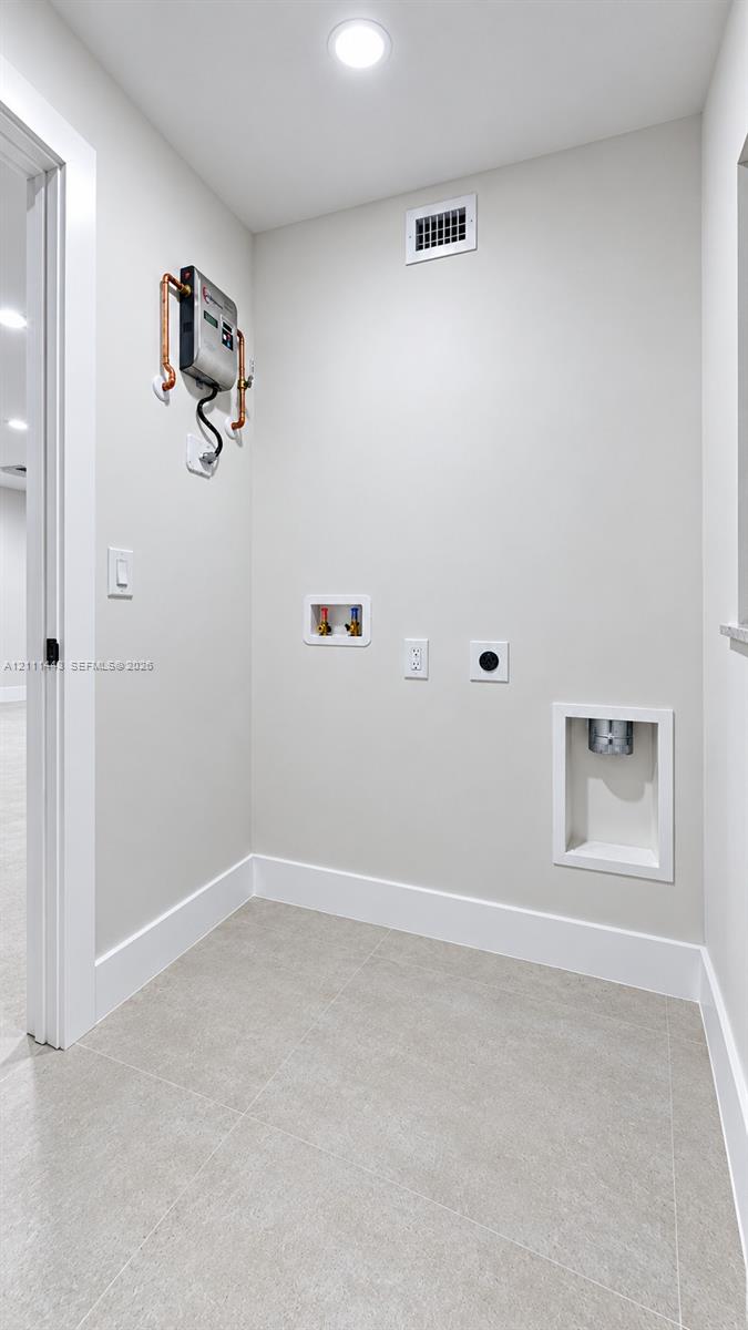 Utility area featuring neutral tile flooring, recessed dryer vent, wall-mounted water shut-off valves, and recessed plumbing hookups