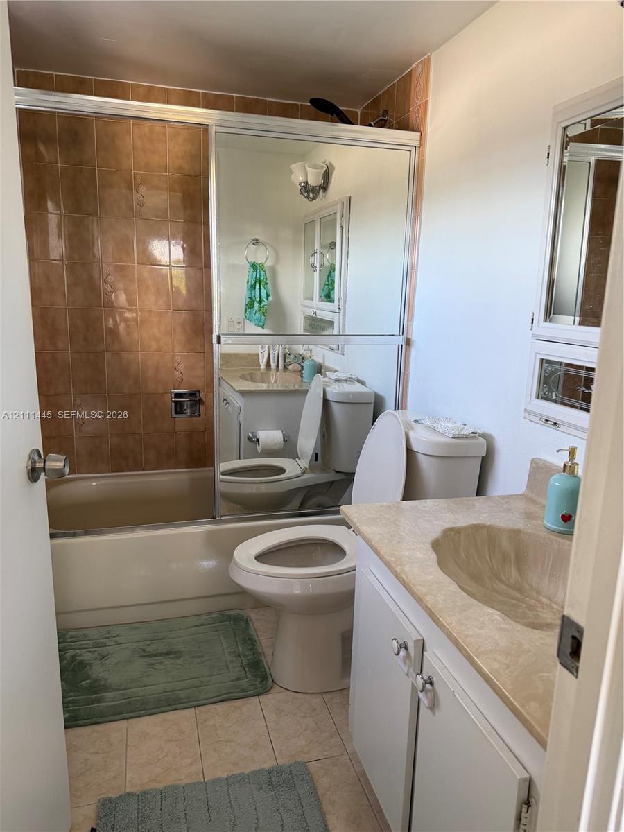 Bathroom featuring a shower-tub combination with tiled surround, sliding glass door, vanity with integrated sink, and medicine cabinet