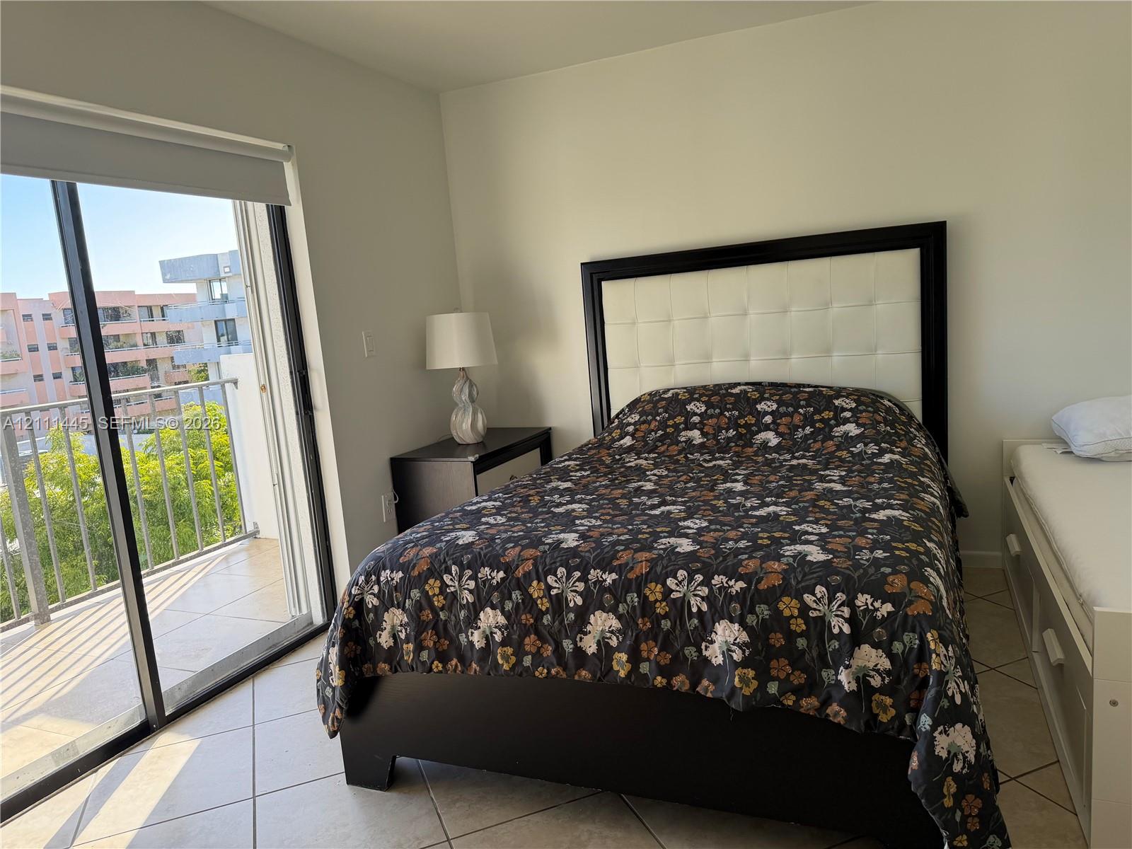Sliding glass door opening to a private balcony with metal railing, neutral tile flooring, and light-toned wall finishes