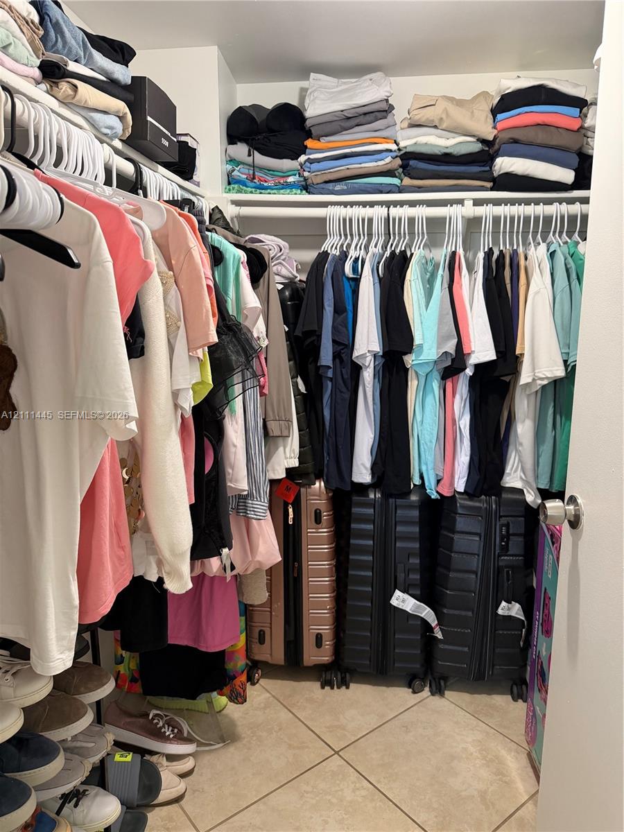 Reach-in closet featuring multi-level hanging rods, upper shelving, and tile flooring