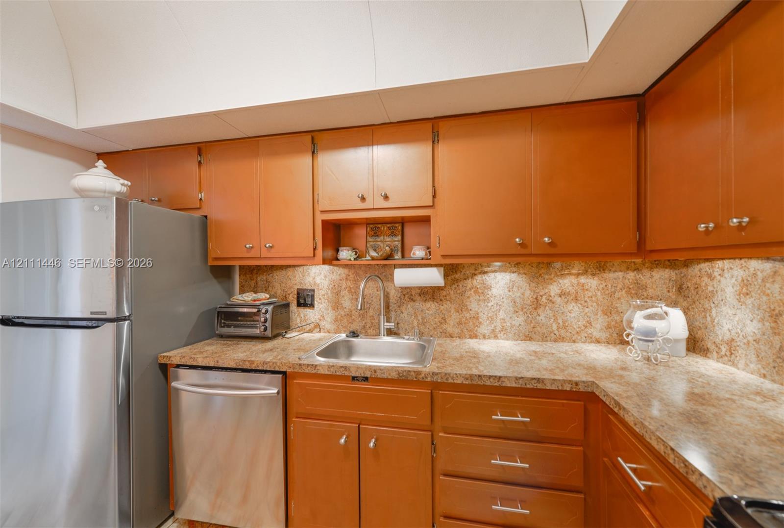Kitchen featuring wood cabinetry, stone-finish countertops, stainless steel appliances, a drop-in stainless steel sink, and a stone-finish backsplash