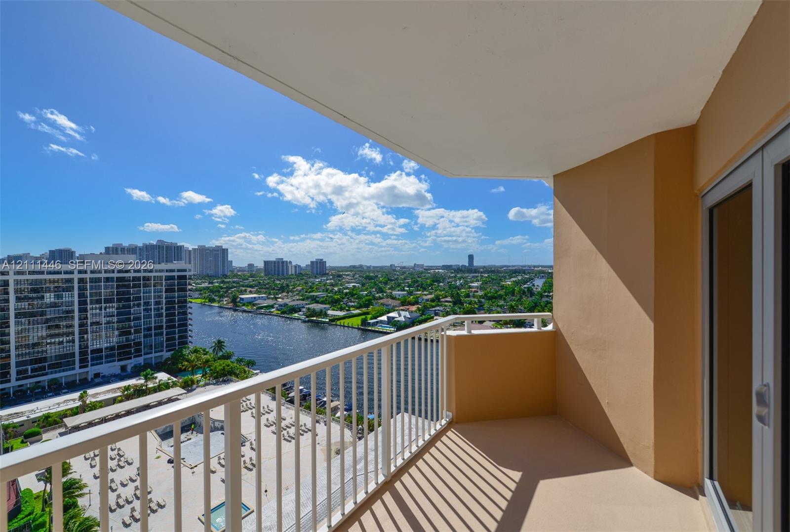 Covered balcony featuring a white metal railing and concrete flooring, overlooking the waterway and urban landscape