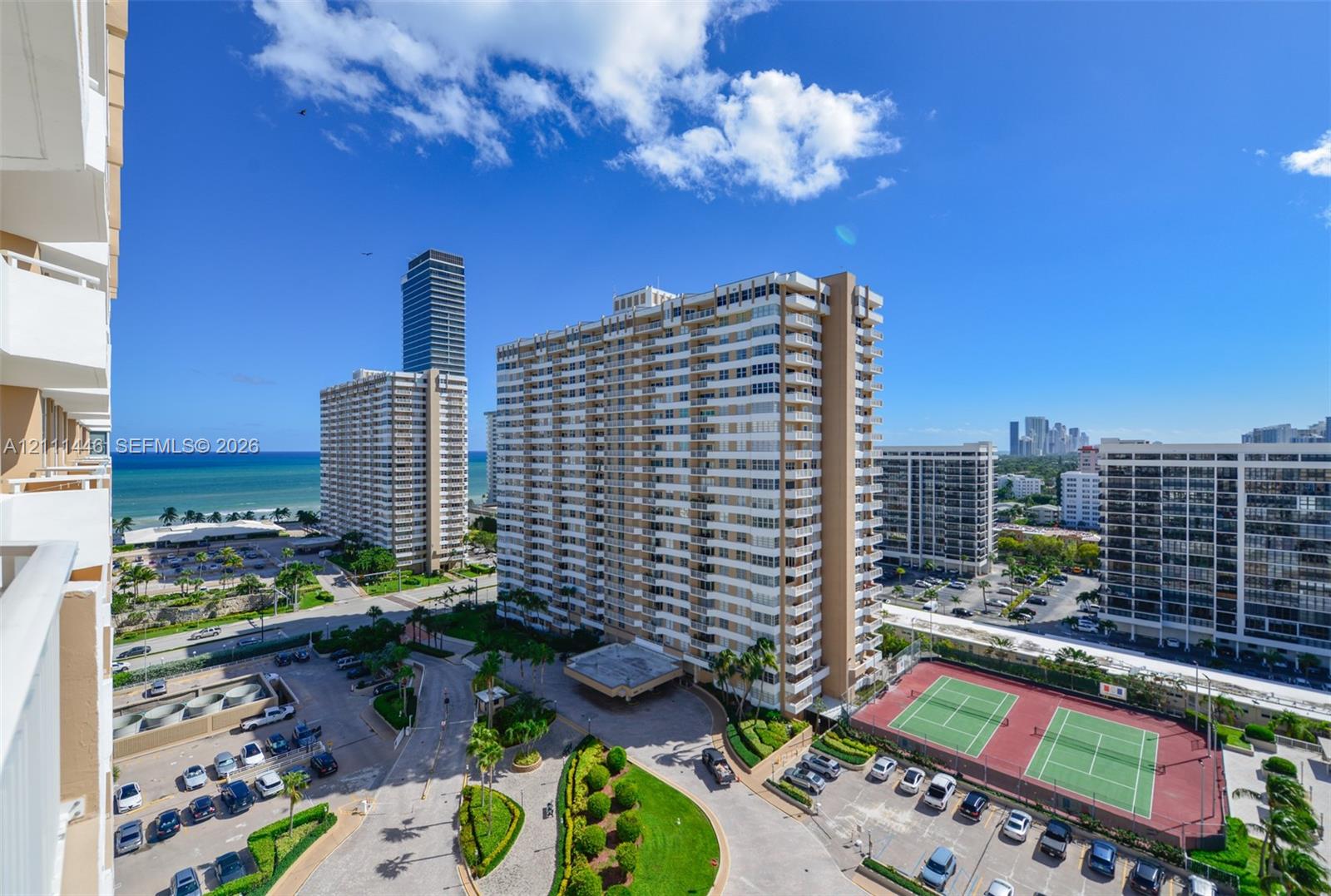 High-rise residential exterior with multi-level private balconies, outdoor tennis courts, landscaped grounds, and proximity to the coastline
