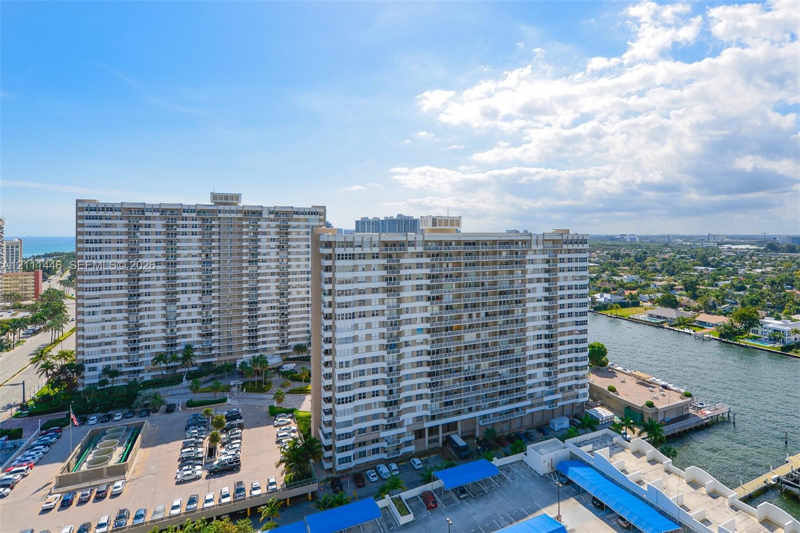 High-rise residential complex featuring private balcony tiers, covered surface parking structures, waterfront positioning, and integrated exterior lighting