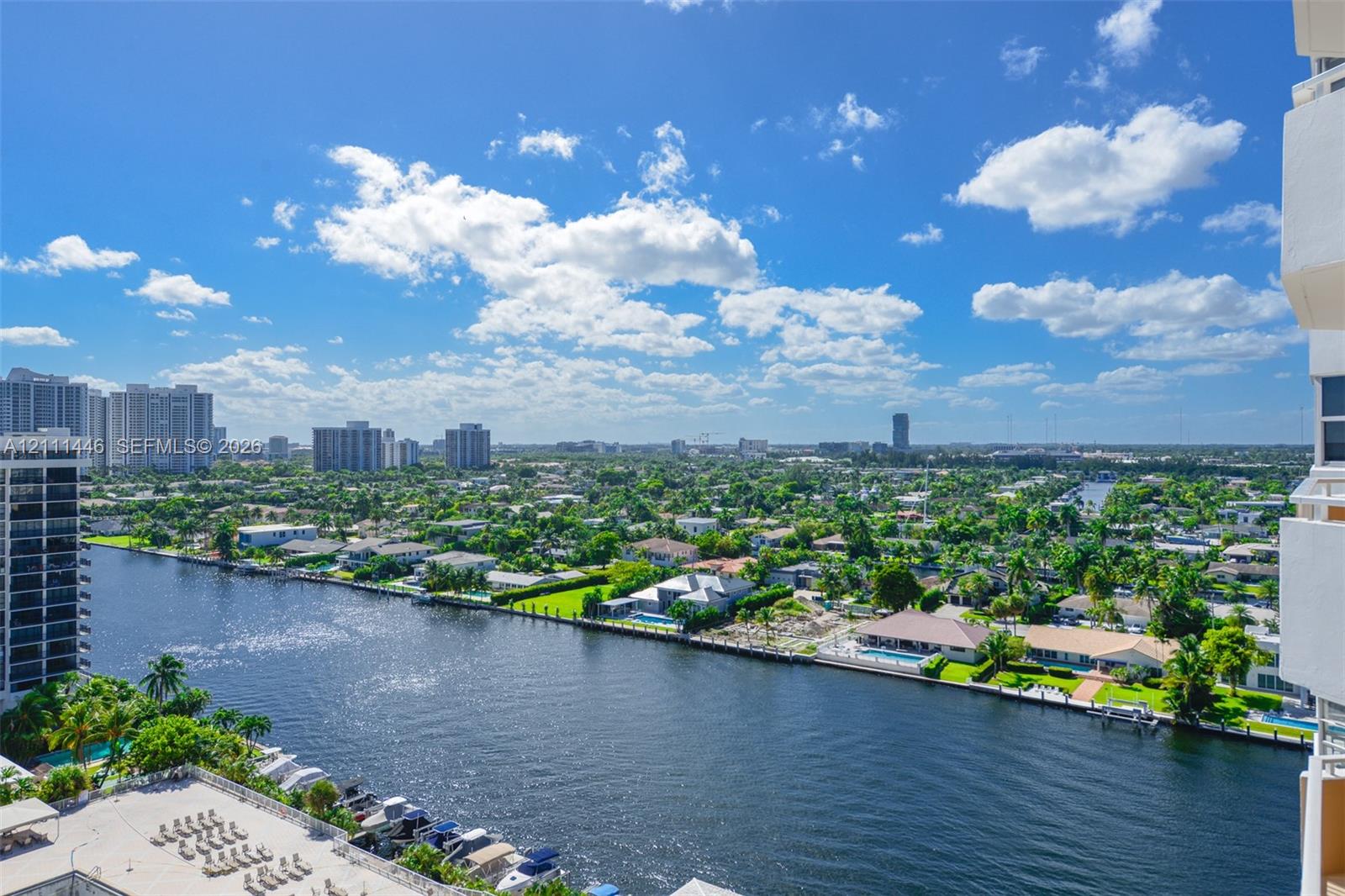 Elevated exterior vantage point featuring an expansive waterway, multiple boat slips, manicured landscape, and an urban skyline