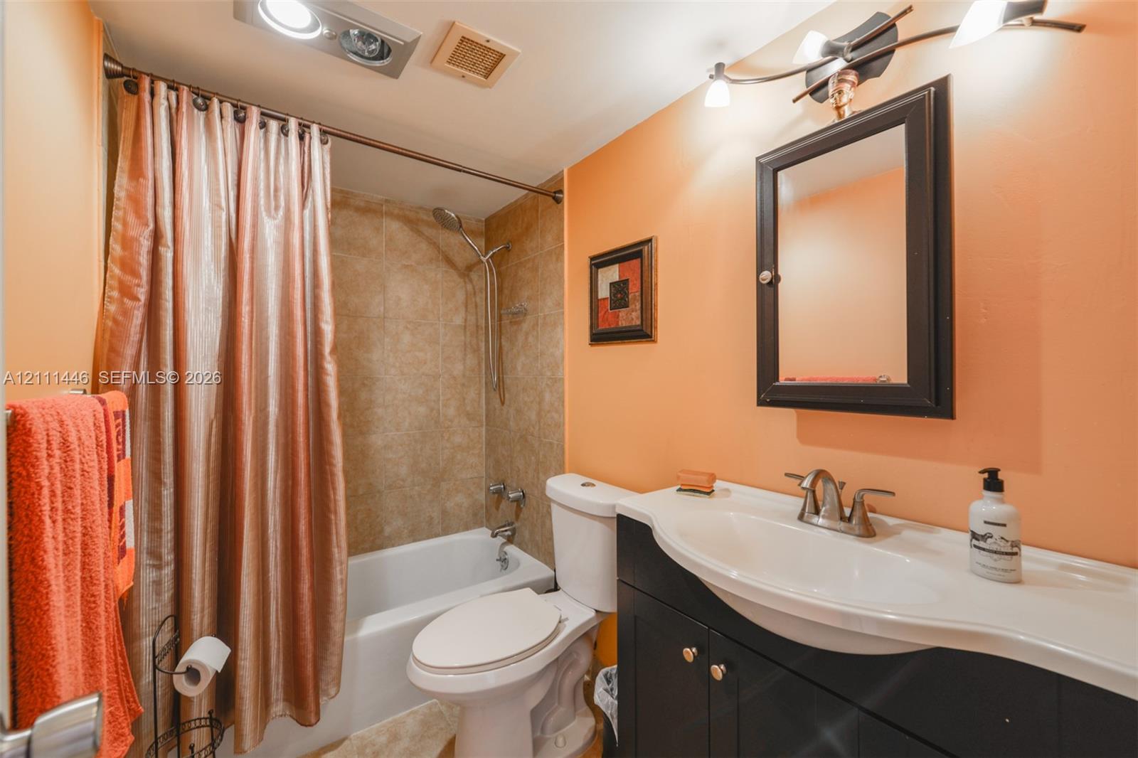 Bathroom featuring a dark wood-finish vanity with a molded countertop, integrated sink, wall-mounted medicine cabinet, and a shower-tub combination with tile surround