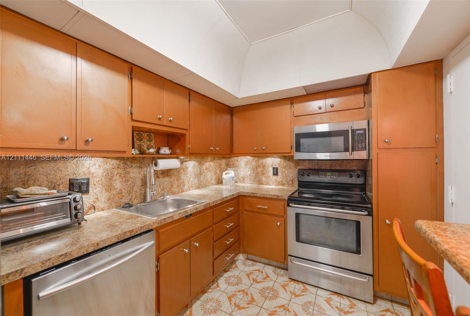 Kitchen featuring wood cabinetry, stainless steel appliances, patterned flooring, recessed lighting, and a vaulted ceiling