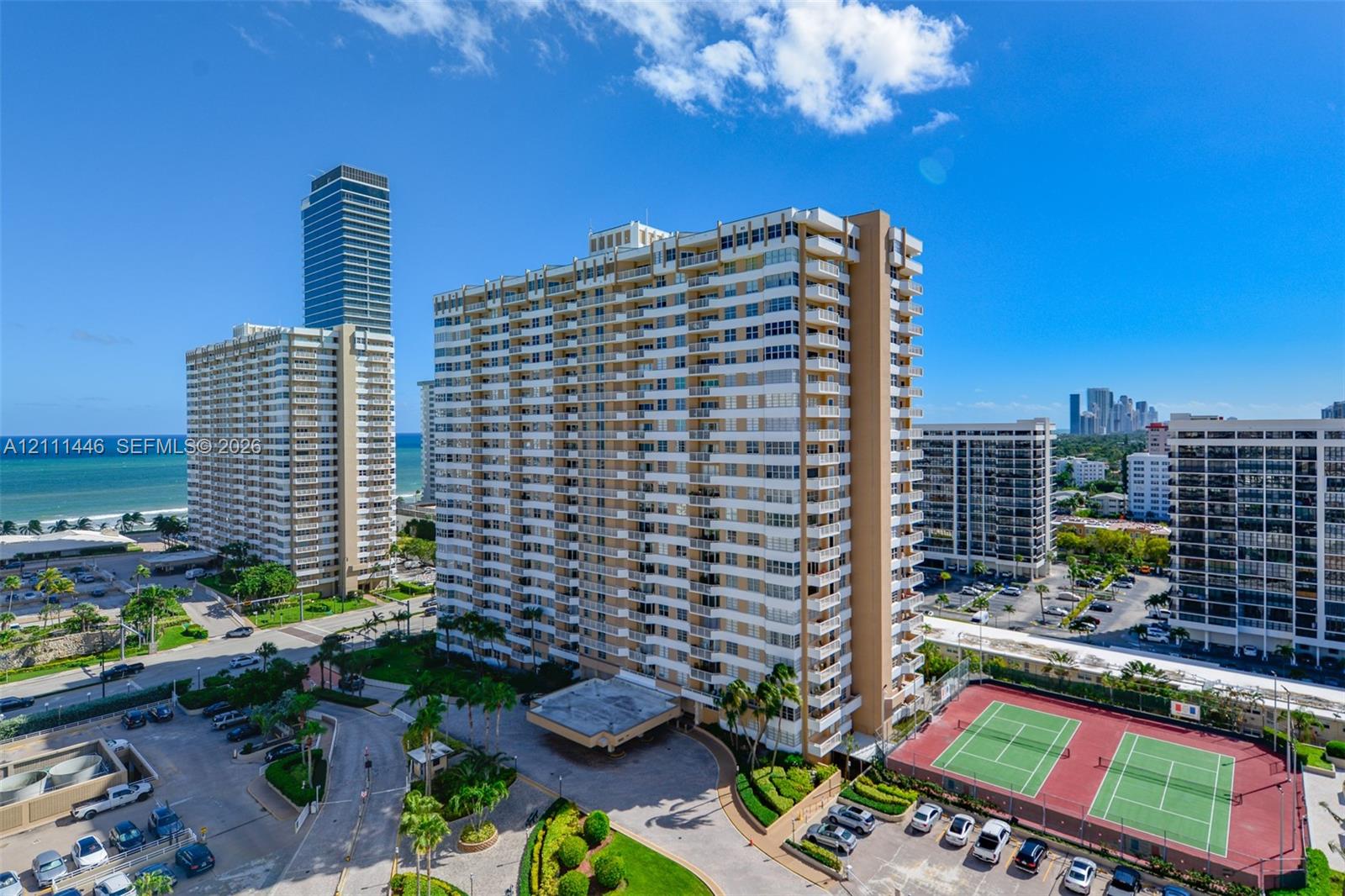 High-rise residential building featuring multiple private balconies, a covered porte-cochre entry, and dual outdoor tennis courts
