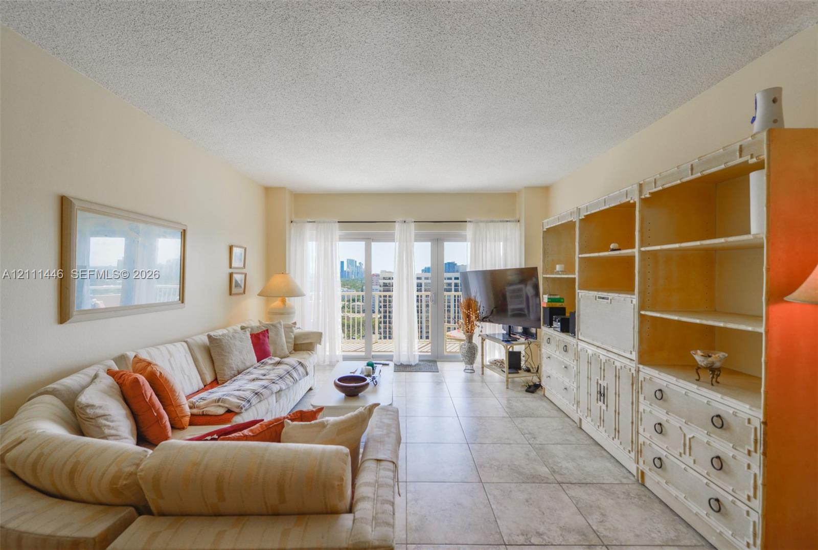 Living area featuring large-format neutral floor tile, built-in floor-to-ceiling cabinetry, and glass paneled doors providing exterior access