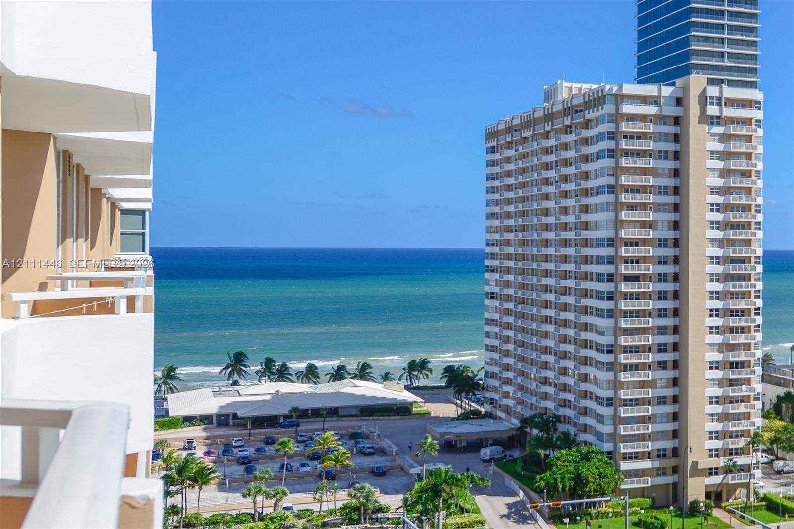 Elevated balcony featuring a white railing and exterior building facade with ocean and coastal scenery