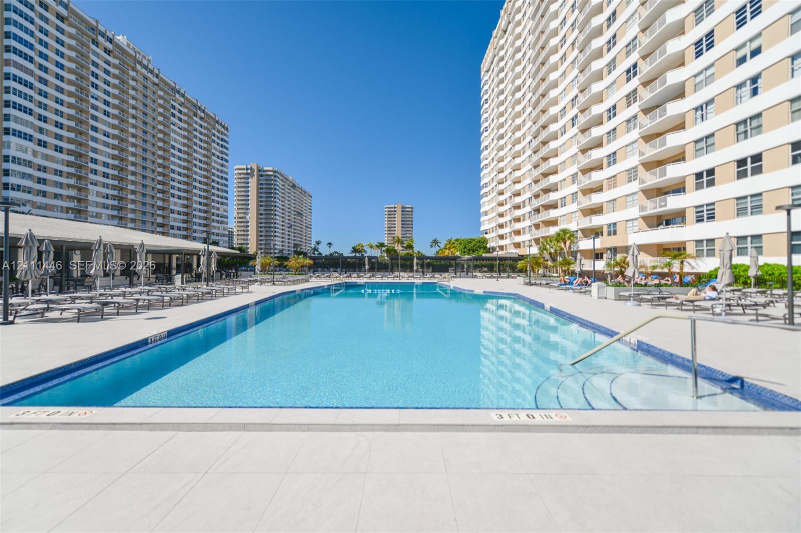 Rectangular swimming pool featuring tile coping, built-in entry steps with a metal handrail, and a surrounding paved pool deck