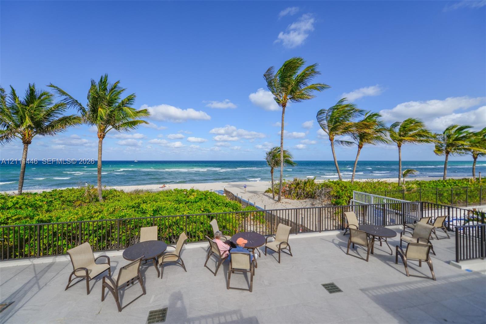 Elevated stone-paved terrace featuring dark metal railings, tropical palm trees, and an open expanse of oceanfront