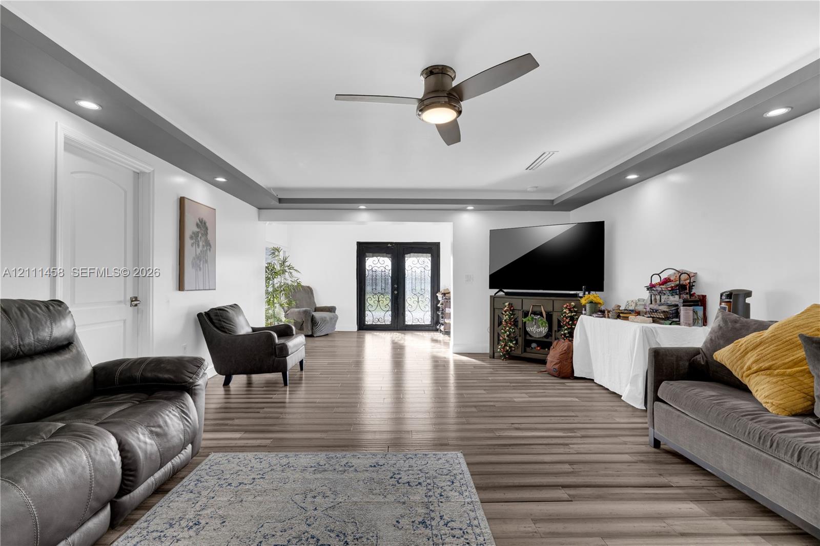 Interior space featuring tray ceiling with recessed lighting, double entry doors with decorative iron detailing, and a central ceiling fan