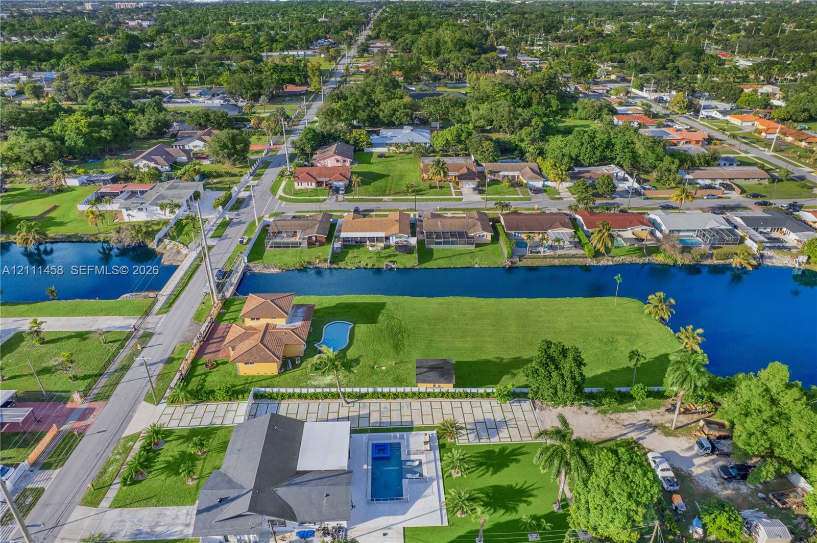 Aerial perspective of a waterfront property featuring a canal-front bulkhead, expansive lawn, swimming pool, and concrete paver driveway
