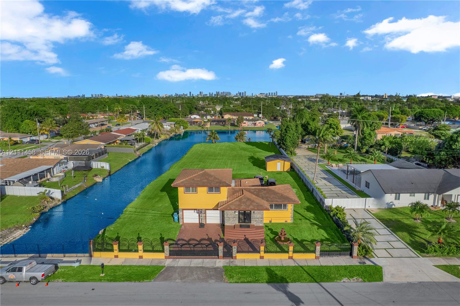 Waterfront residential property featuring expansive lawn space, decorative perimeter fencing, concrete driveway, and attached garage Waterfront residential property featuring expansive lawn space, decorative perimeter fencing, concrete driveway, and attached garage