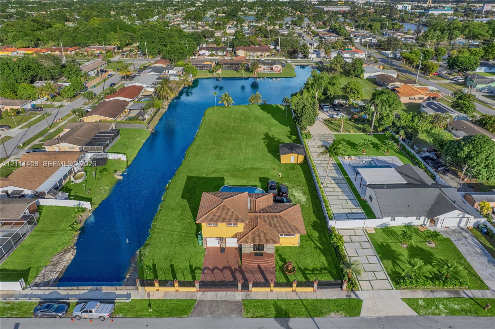 Aerial view featuring a waterfront lot, an in-ground swimming pool, a multi-story residence with a tiled roof, and a paved driveway