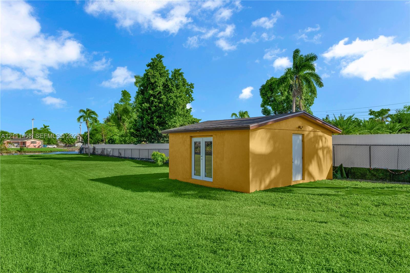 Expansive backyard featuring a manicured lawn, a detached outbuilding, French doors, and perimeter fencing