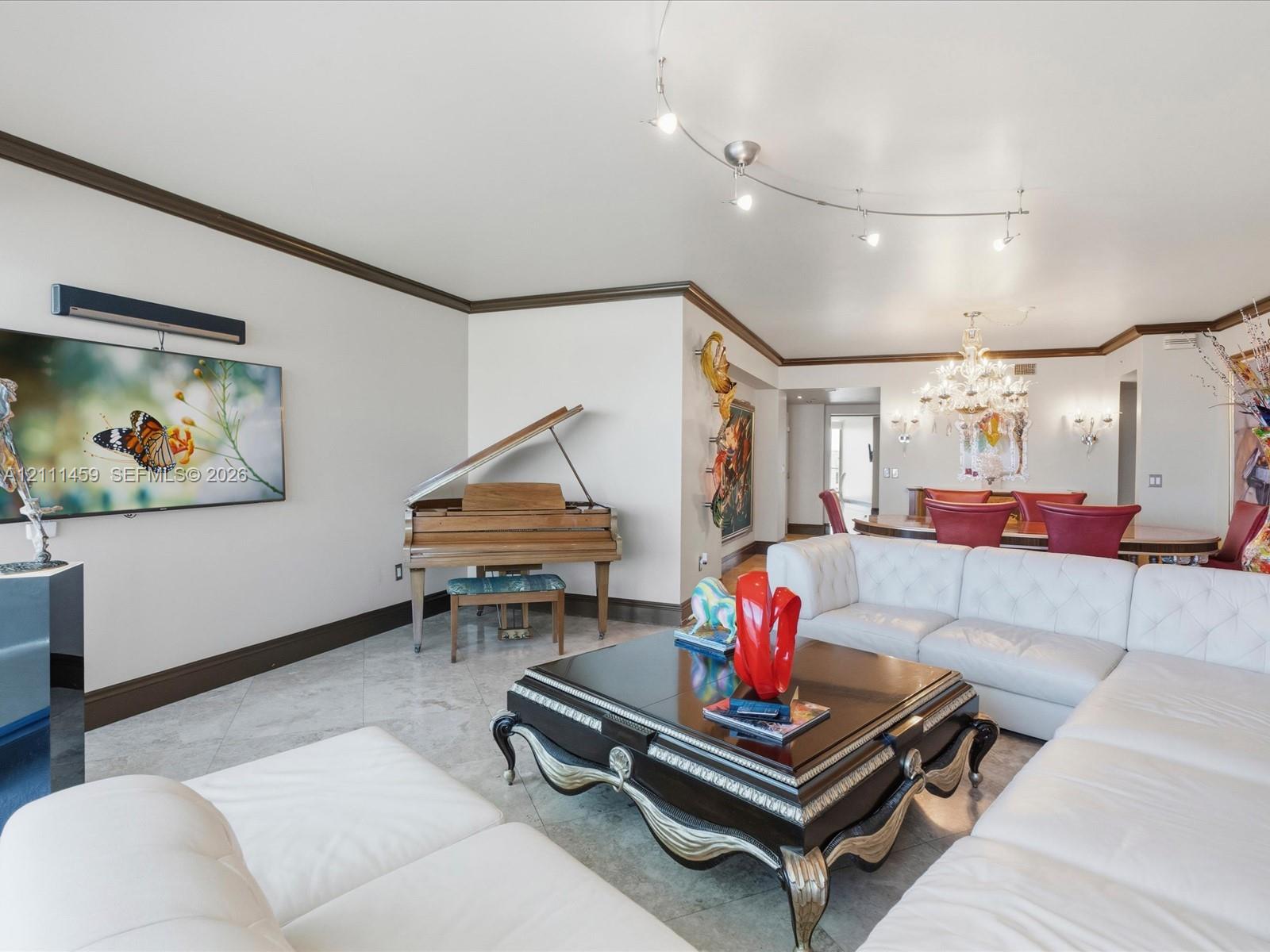 Open living area featuring large-format stone tile flooring, crown molding, arched track lighting, and a crystal chandelier