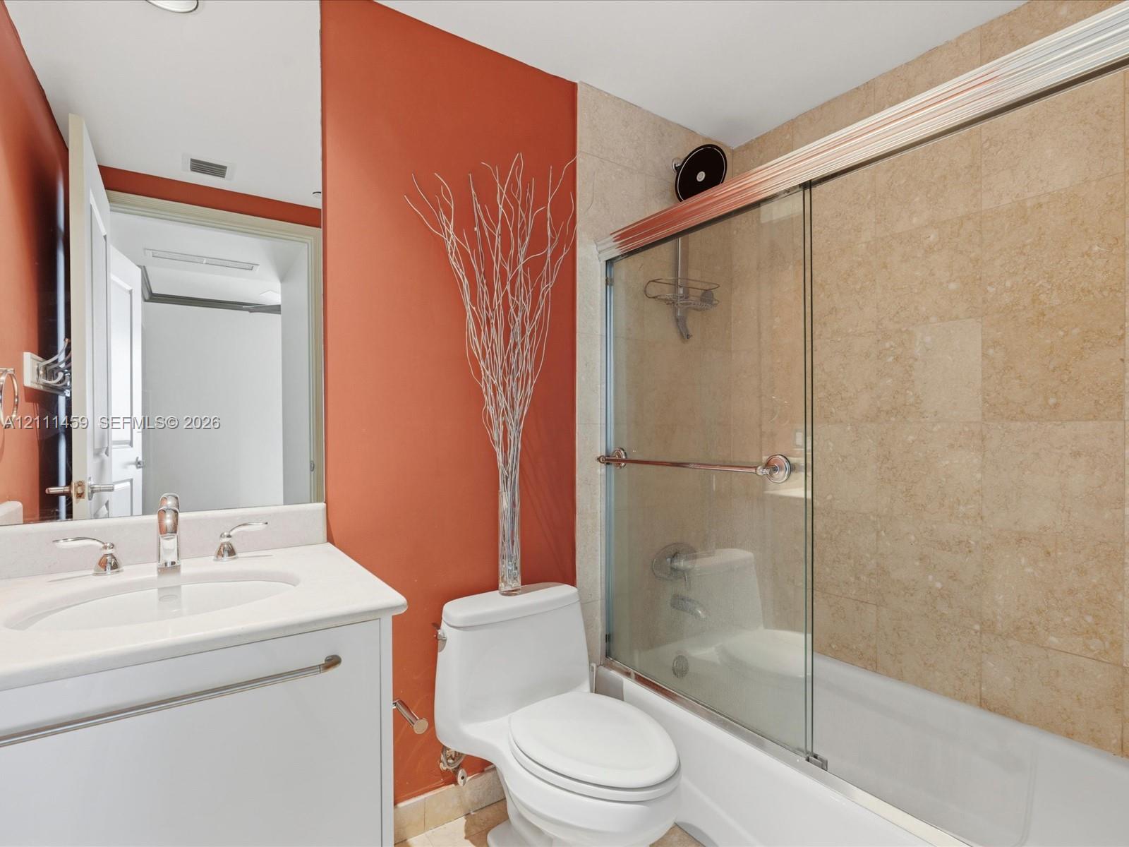 Bathroom featuring a white vanity cabinet with an integrated sink, polished metal widespread faucet, and a shower-tub combination enclosed by glass sliding doors with tiled wall surrounds