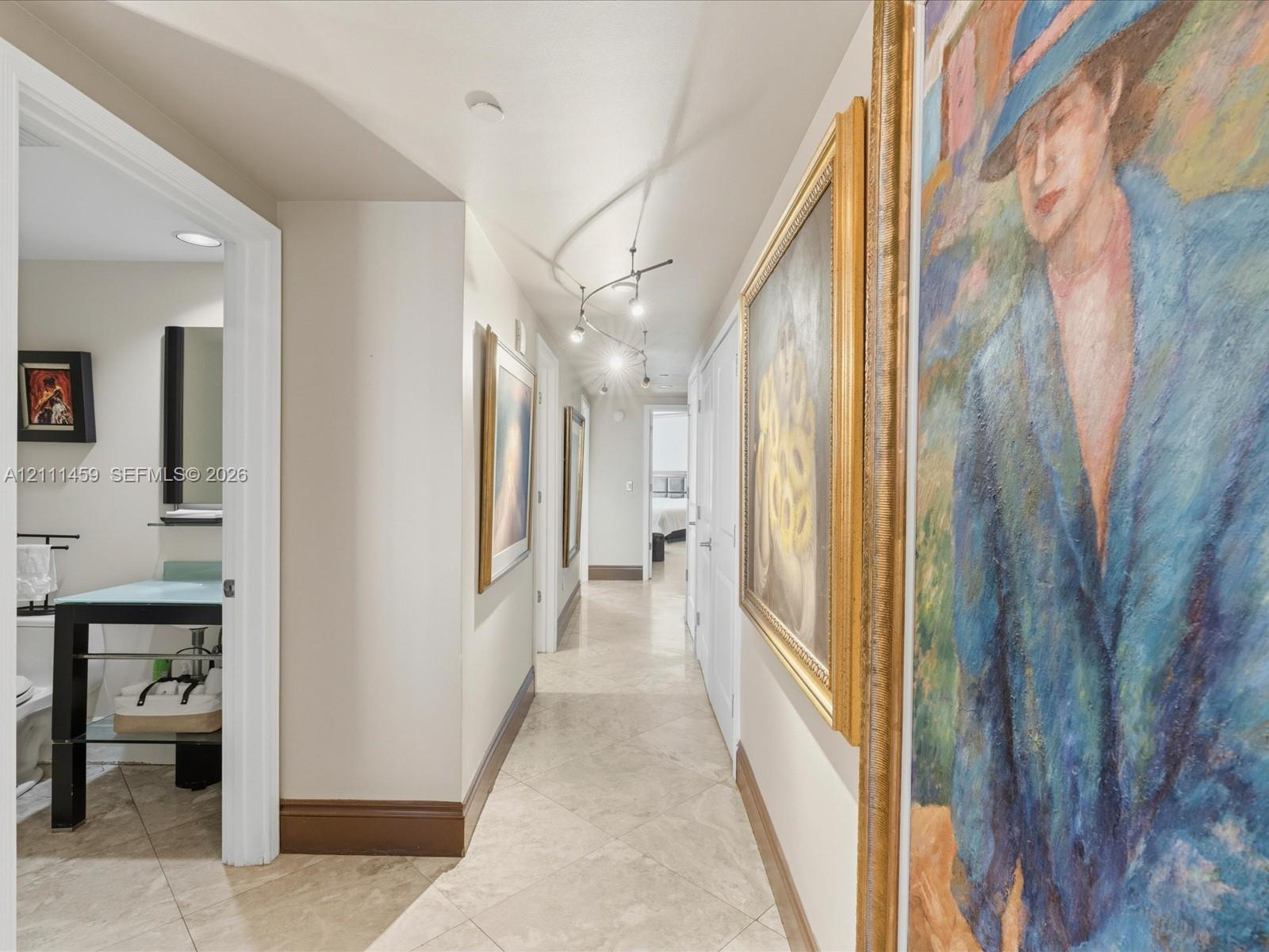 Hallway featuring diagonal-set stone tile flooring, directional track lighting, and a bathroom equipped with a glass-top console vanity