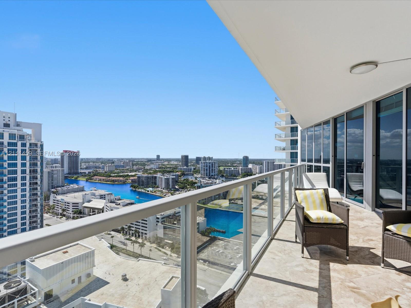 Private balcony featuring stone tile flooring, a glass-panel railing, and an overhead lighting fixture