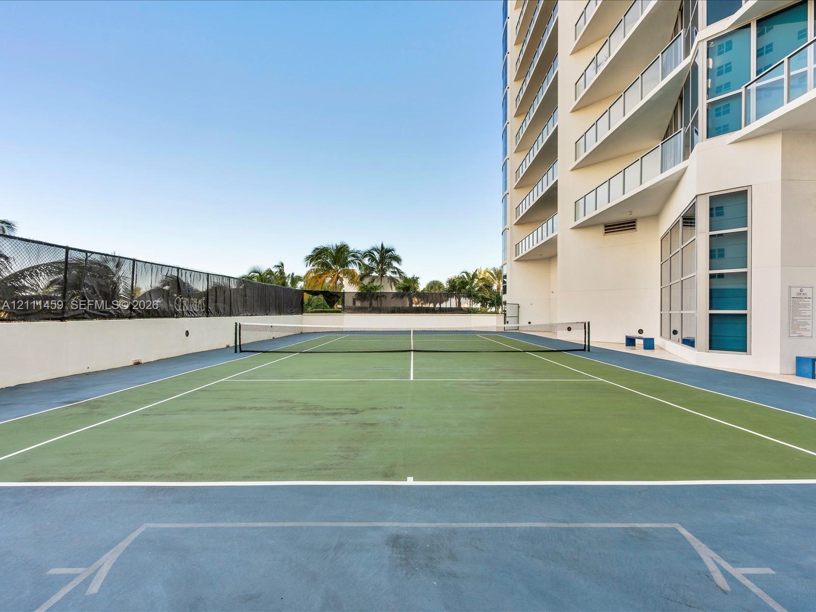 Tennis court featuring a multi-colored hard surface, perimeter fencing, and high-rise building exterior