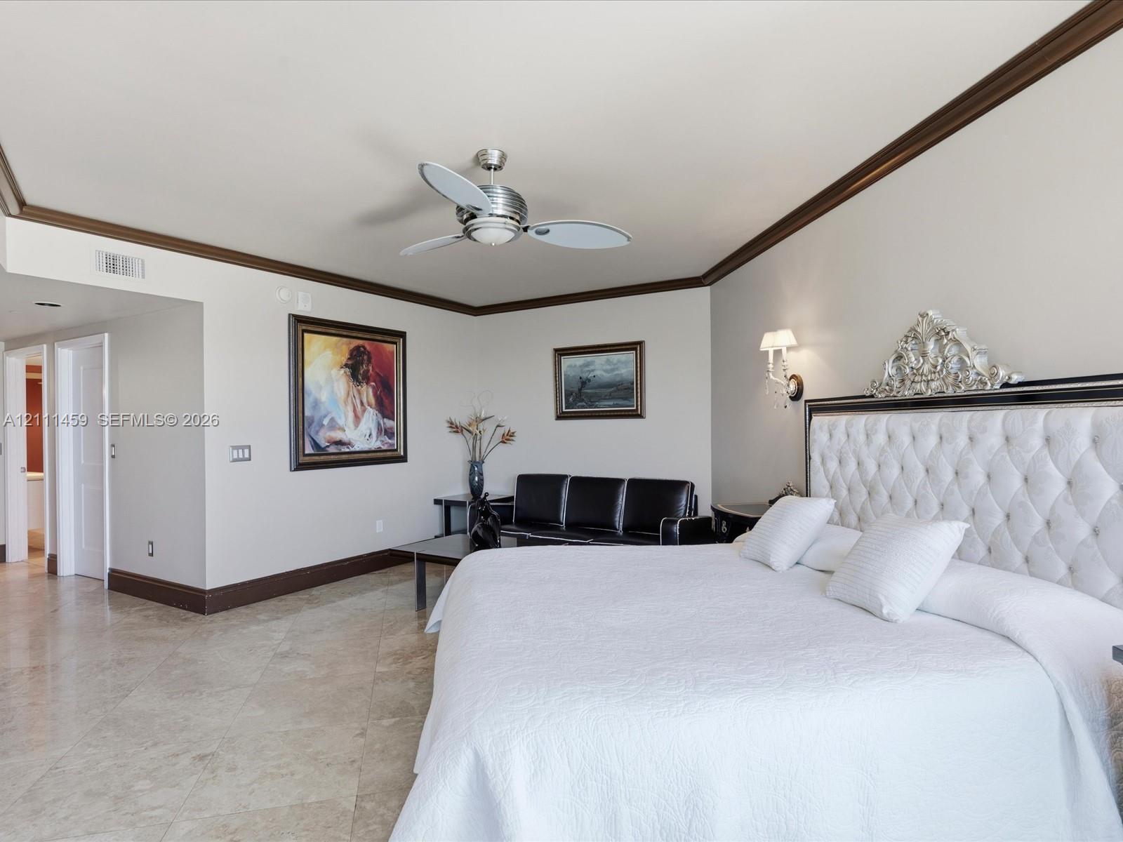 Large room featuring stone flooring, crown molding, wall-mounted light fixtures, and a ceiling fan with integrated lighting