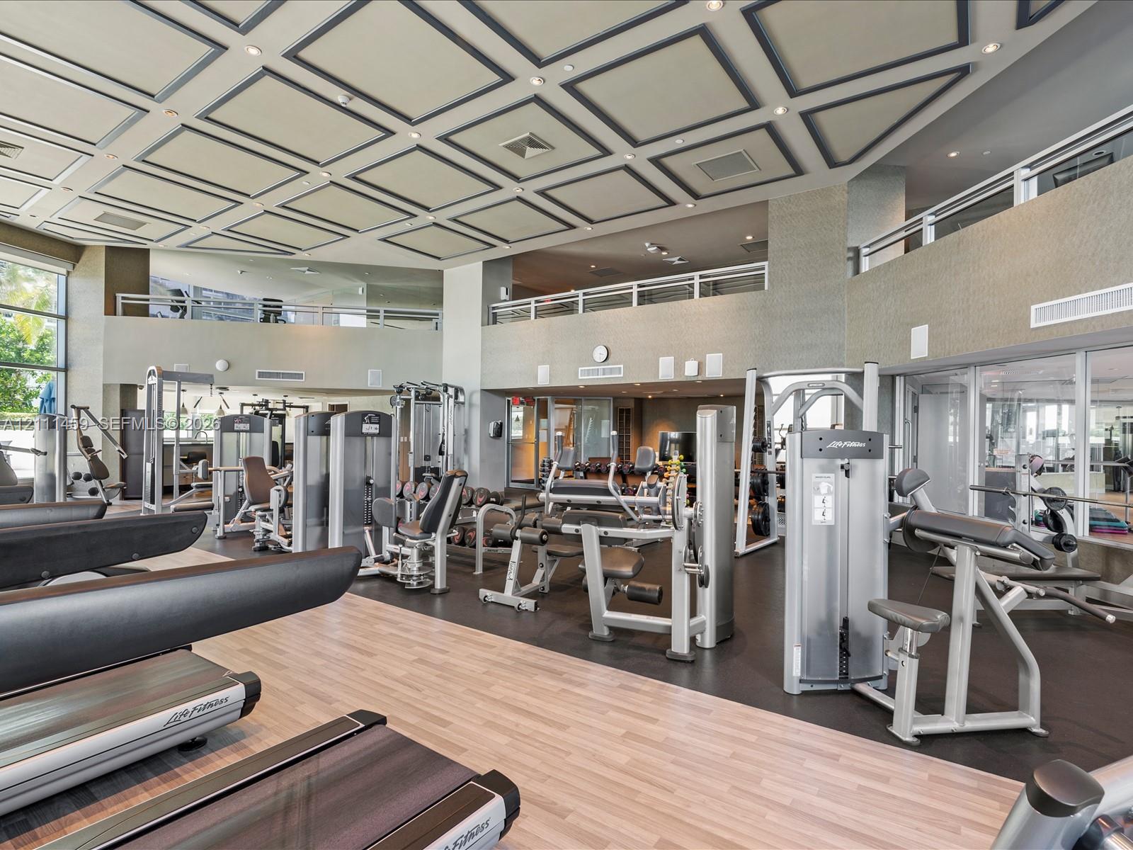 Fitness center featuring a coffered ceiling, wood-finish flooring, recessed lighting, and a mezzanine level with metal railings