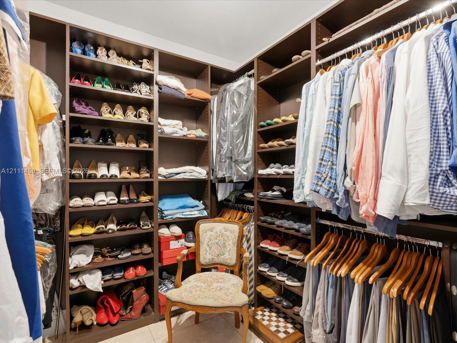 Walk-in closet featuring extensive dark wood-finish cabinetry, floor-to-ceiling adjustable shelving, integrated garment hanging rods, and tile flooring