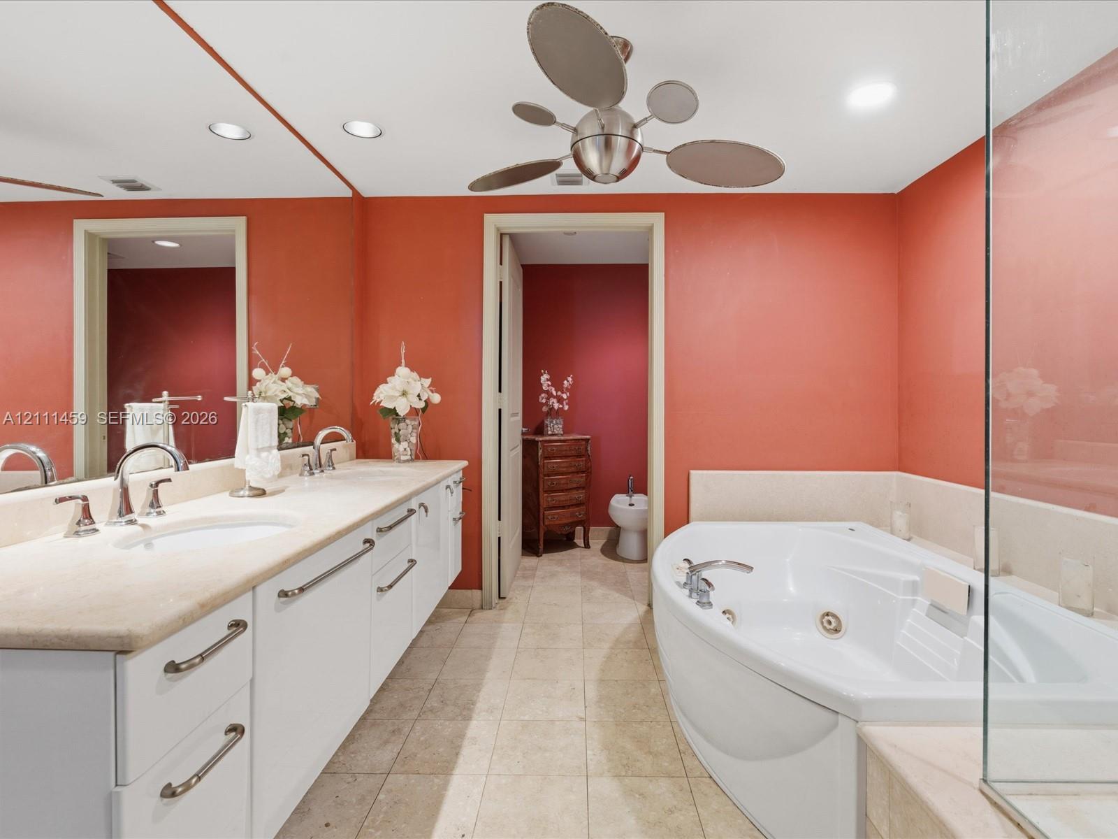 Dual-sink vanity with stone countertop, recessed lighting, jetted soaking tub, glass-enclosed shower, and stone-finish flooring