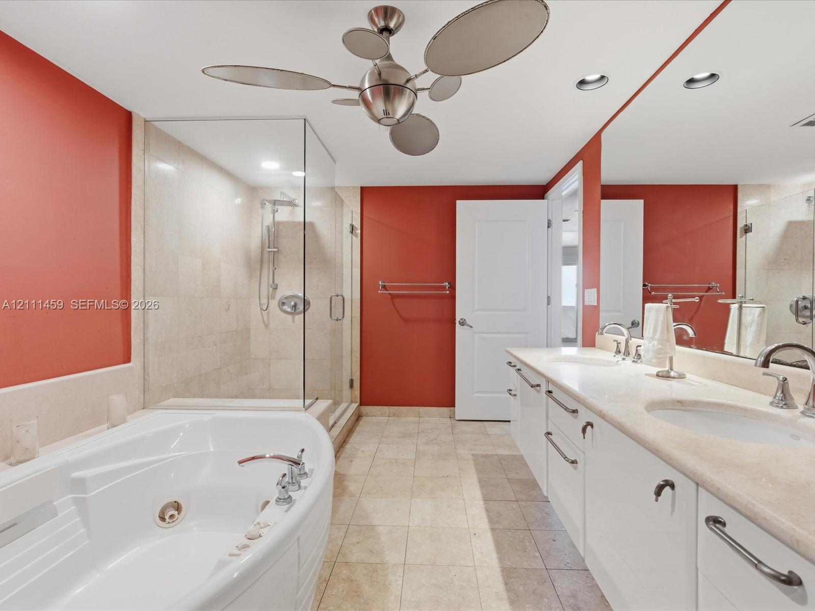 Dual-sink vanity with stone countertop, jetted soaking tub, glass-enclosed shower with tile surround, and brushed-finish ceiling fan