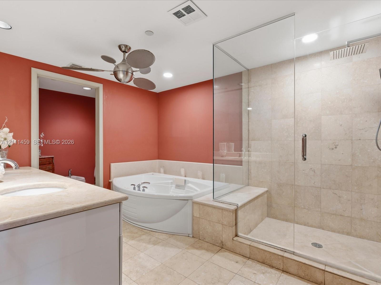 Bathroom featuring a glass-enclosed shower with stone tile surround, a built-in jetted soaking tub, a stone-topped vanity, and recessed lighting
