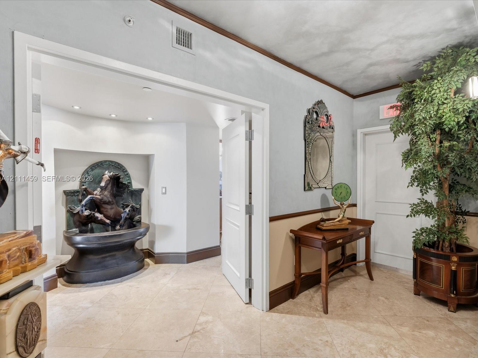 Entryway featuring stone tile flooring, crown molding, chair rail trim, and a recessed wall niche with a built-in decorative basin