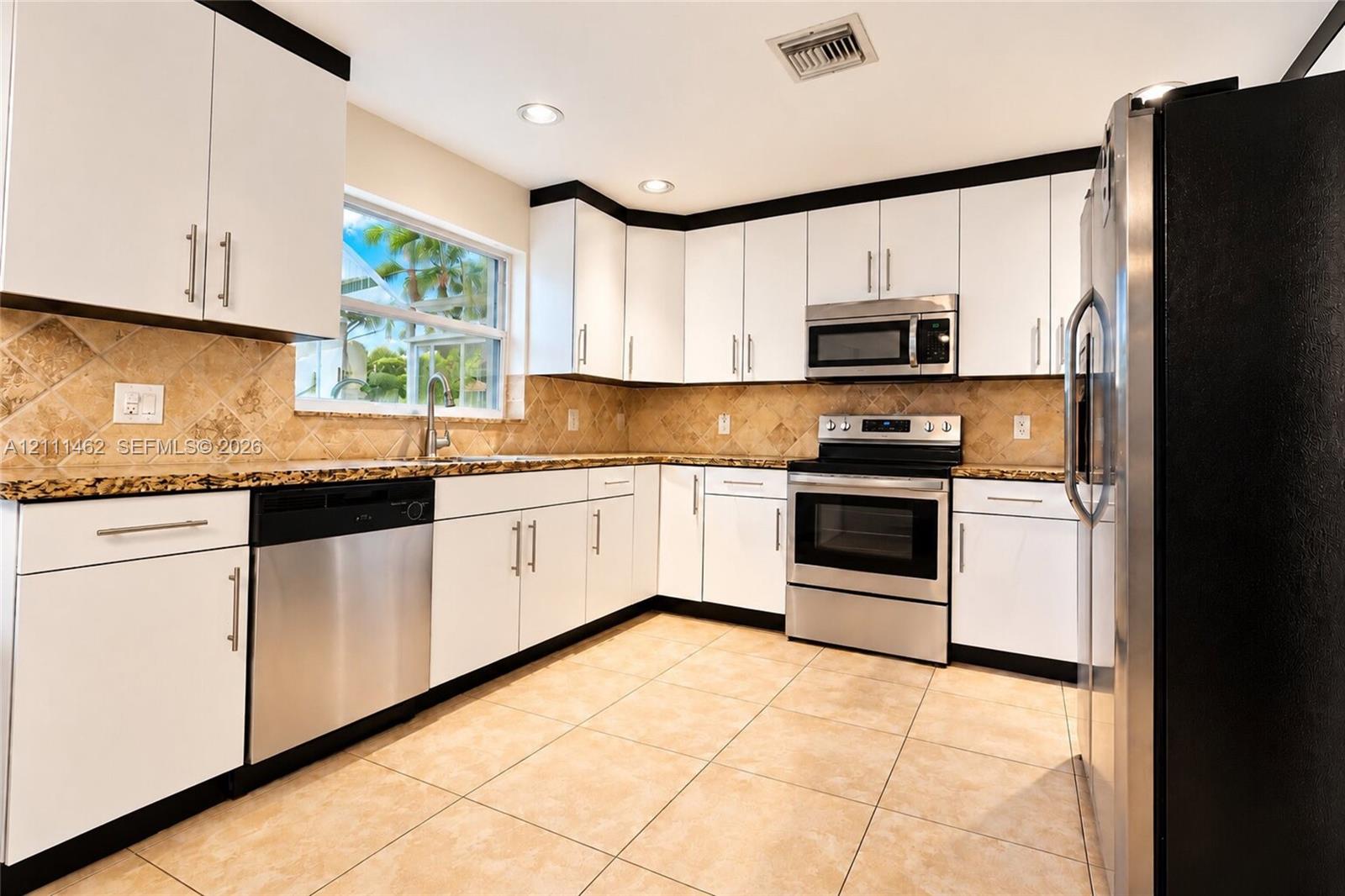 Kitchen featuring white cabinetry with dark crown molding, stone-finish countertops, tile backsplash, stainless steel appliances, and large-format floor tiling