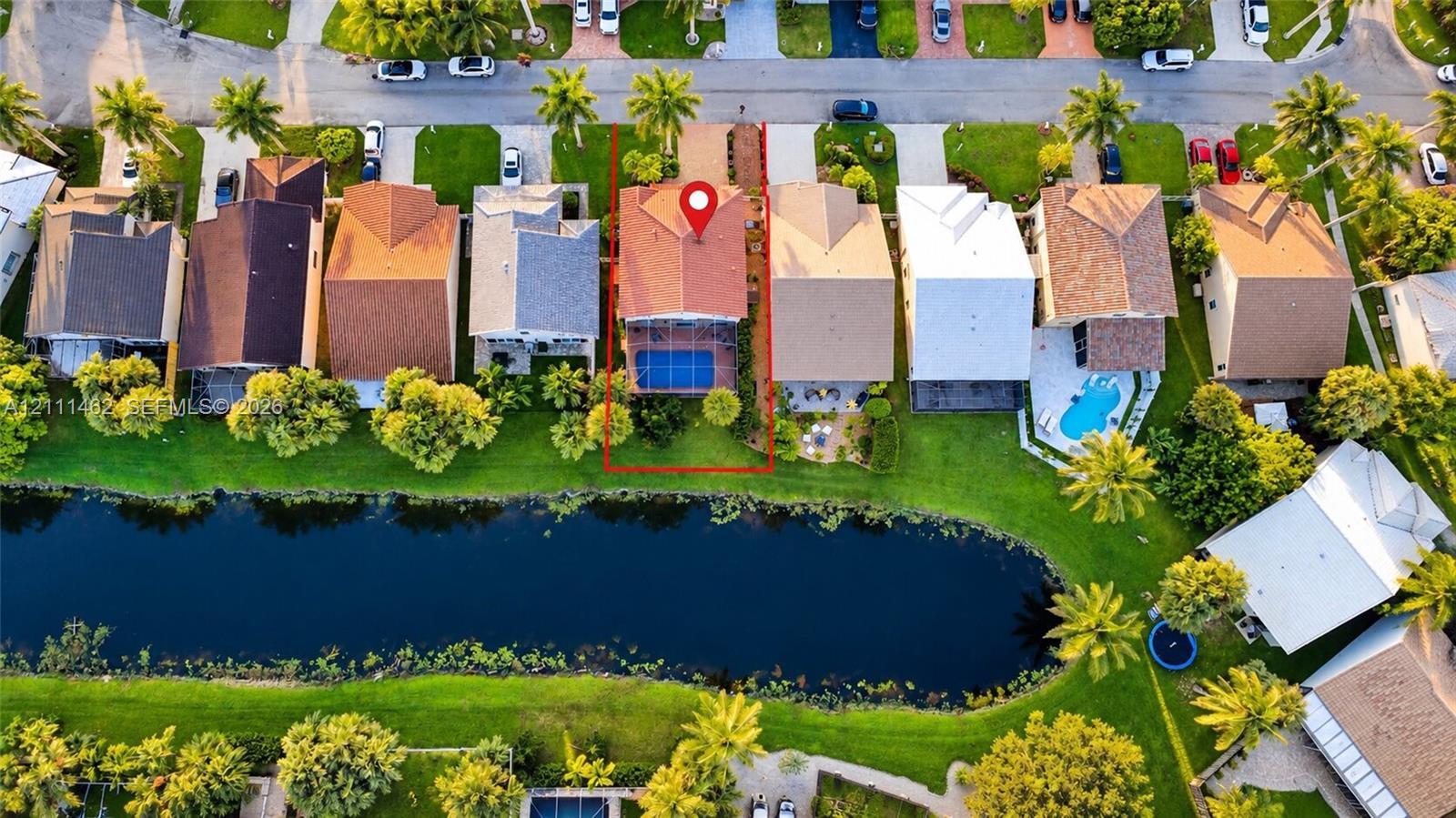 Aerial perspective of a property featuring a tiled roof, screened-in swimming pool, paved patio, and waterfront location