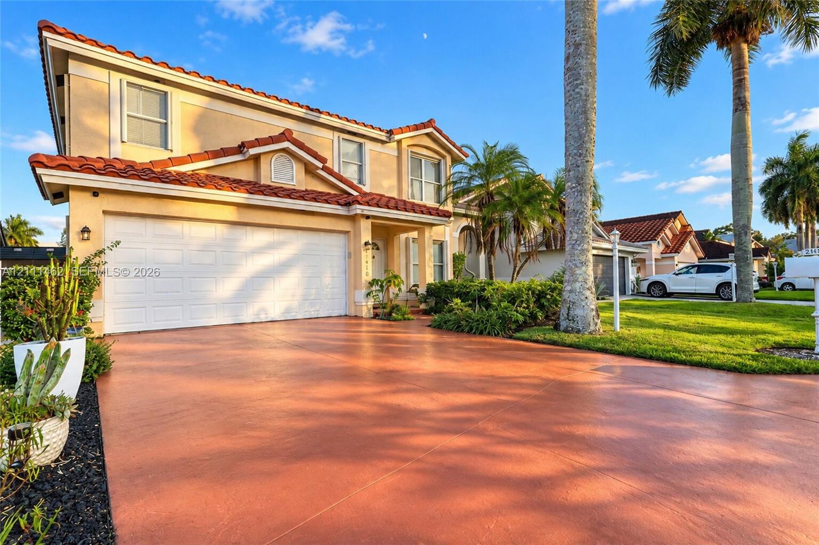 Two-story exterior featuring a clay tile roof, stucco siding, a multi-car garage, and a finished driveway